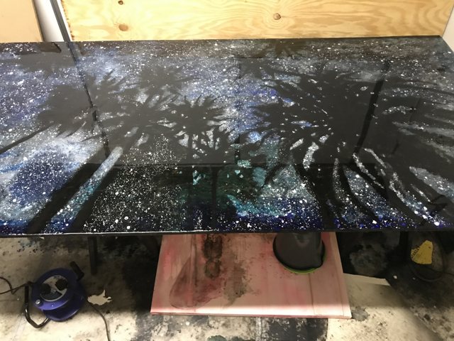 Palm painting in progress on trestles, white spray over a night-dark ground